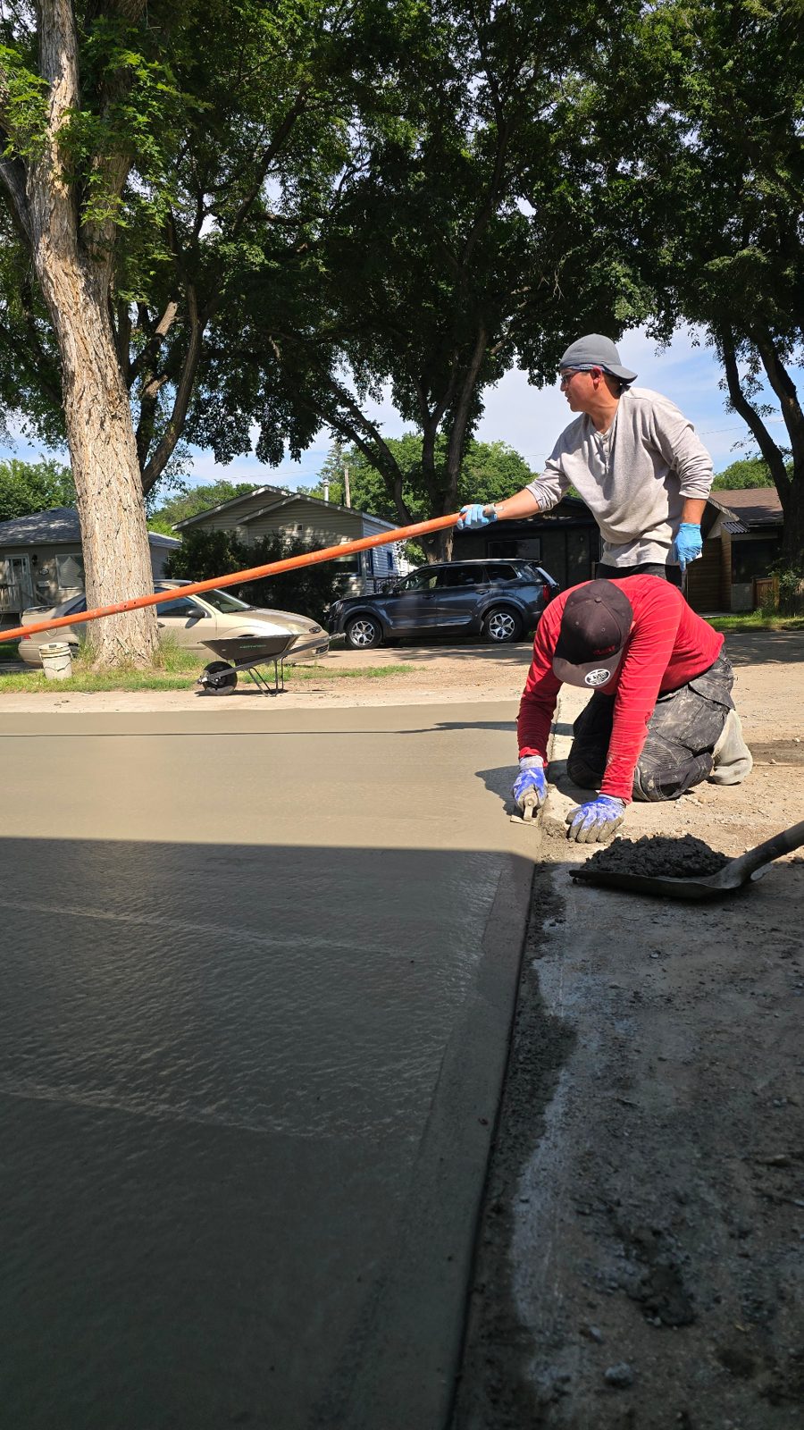 Finisher smoothing the edge of a freshly poured concrete driveway with a bull float overhead