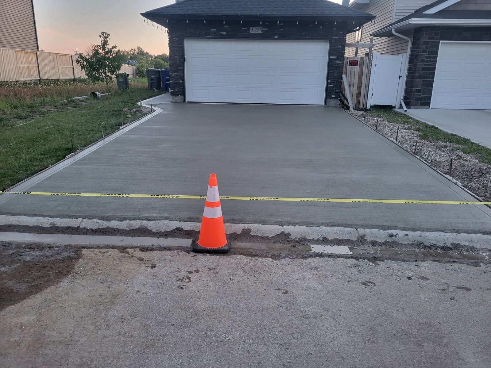 Freshly finished concrete driveway at sunset with safety cone and caution tape